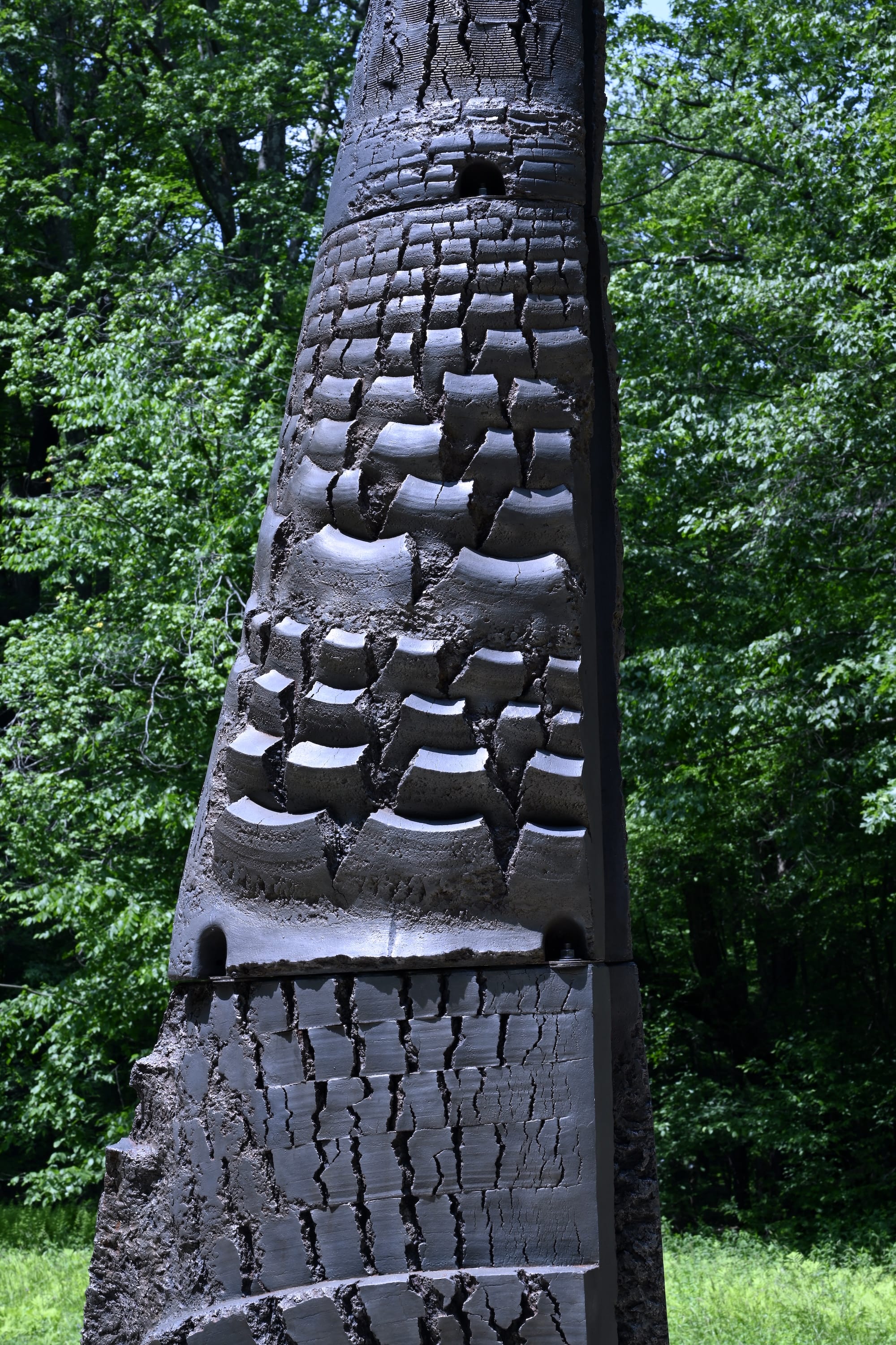 A detail of a conical, structured, black, abstract sculpture of Yō Akiyama installed outdoors