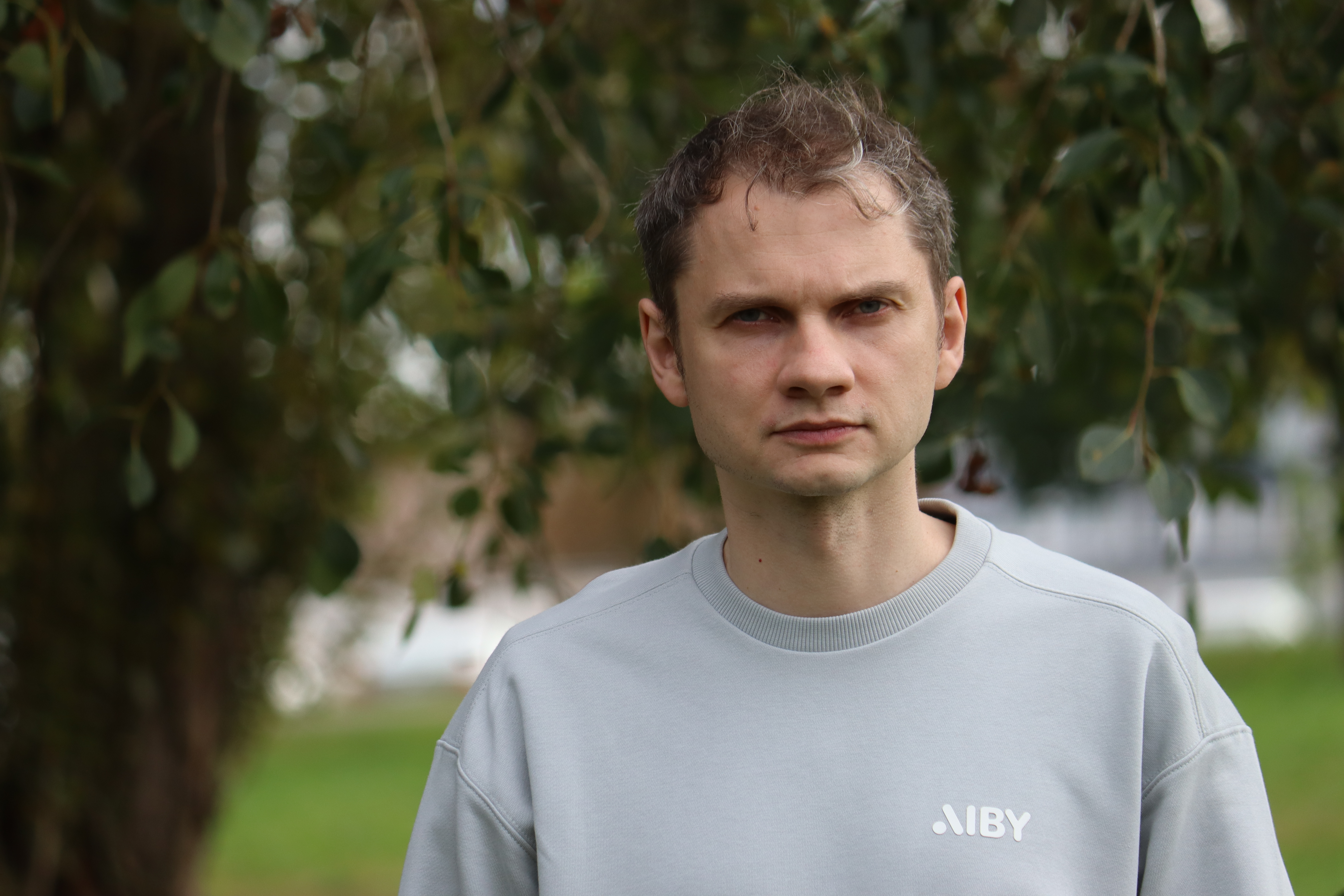 A man's head shot in a gray sweater in front of a tree