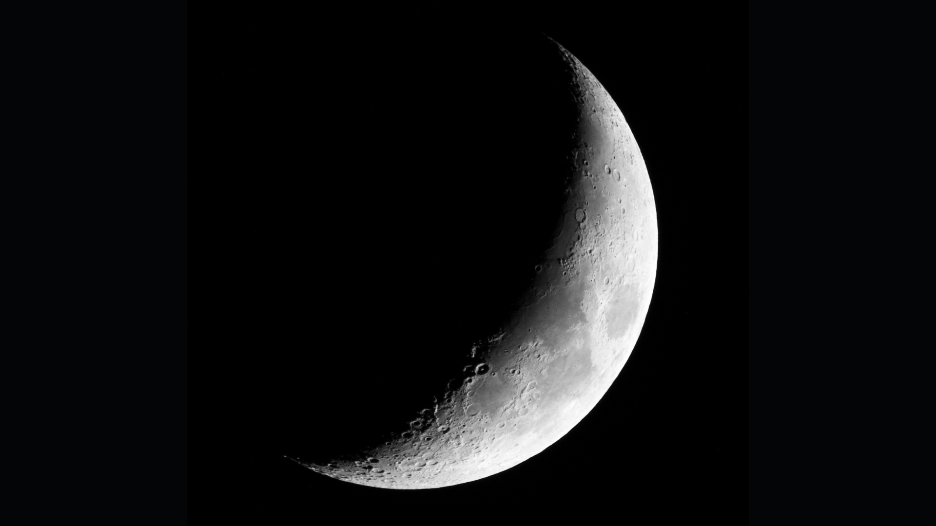 A growing crescent moon is depicted with the right side, which is illuminated by sunlight and is hidden on the left in the shade against a black sky.