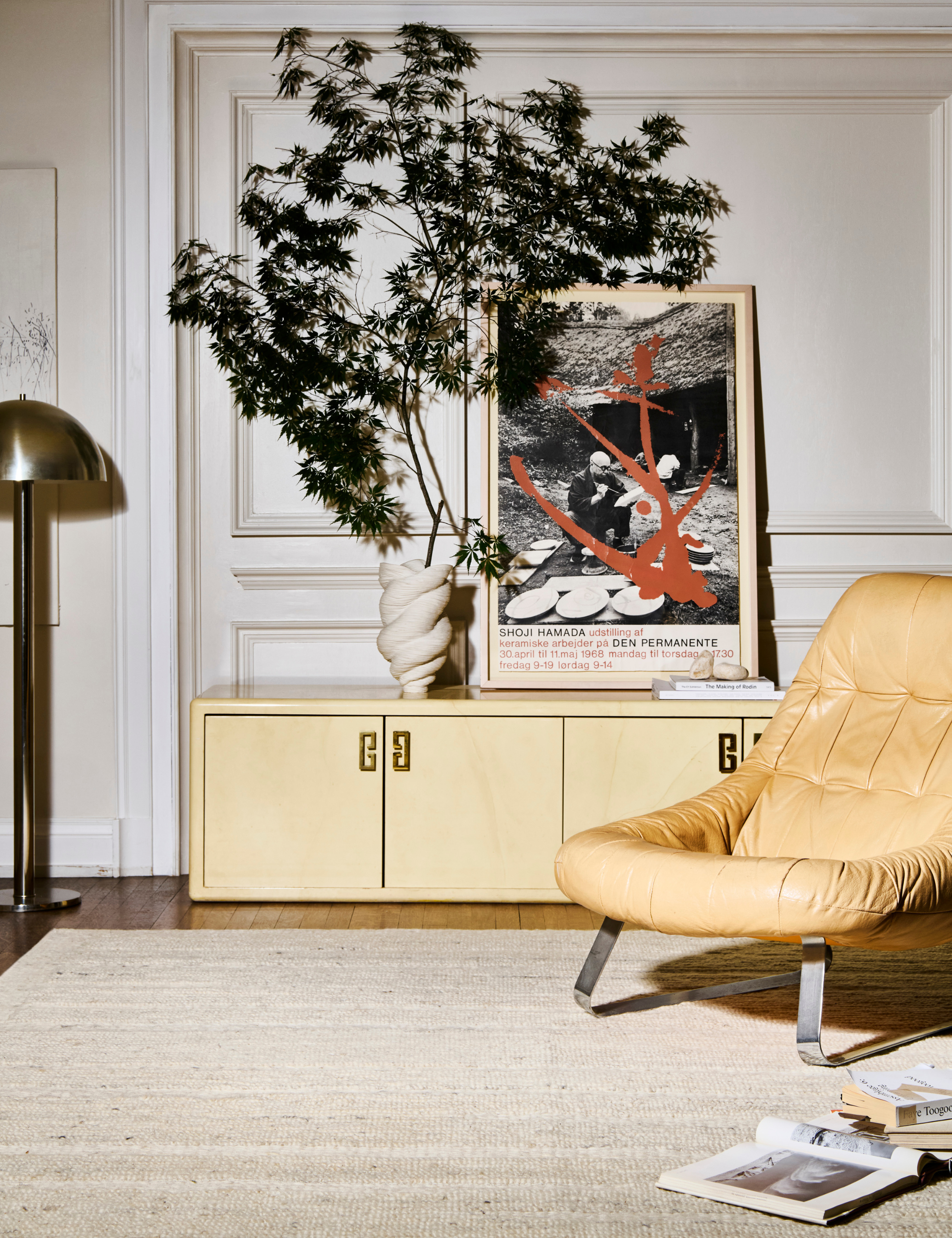 Cream-colored hand-woven rug anchoring a living room with a chrome floor lamp, a butter-yellow ottoman, and a butter-colored credenza.