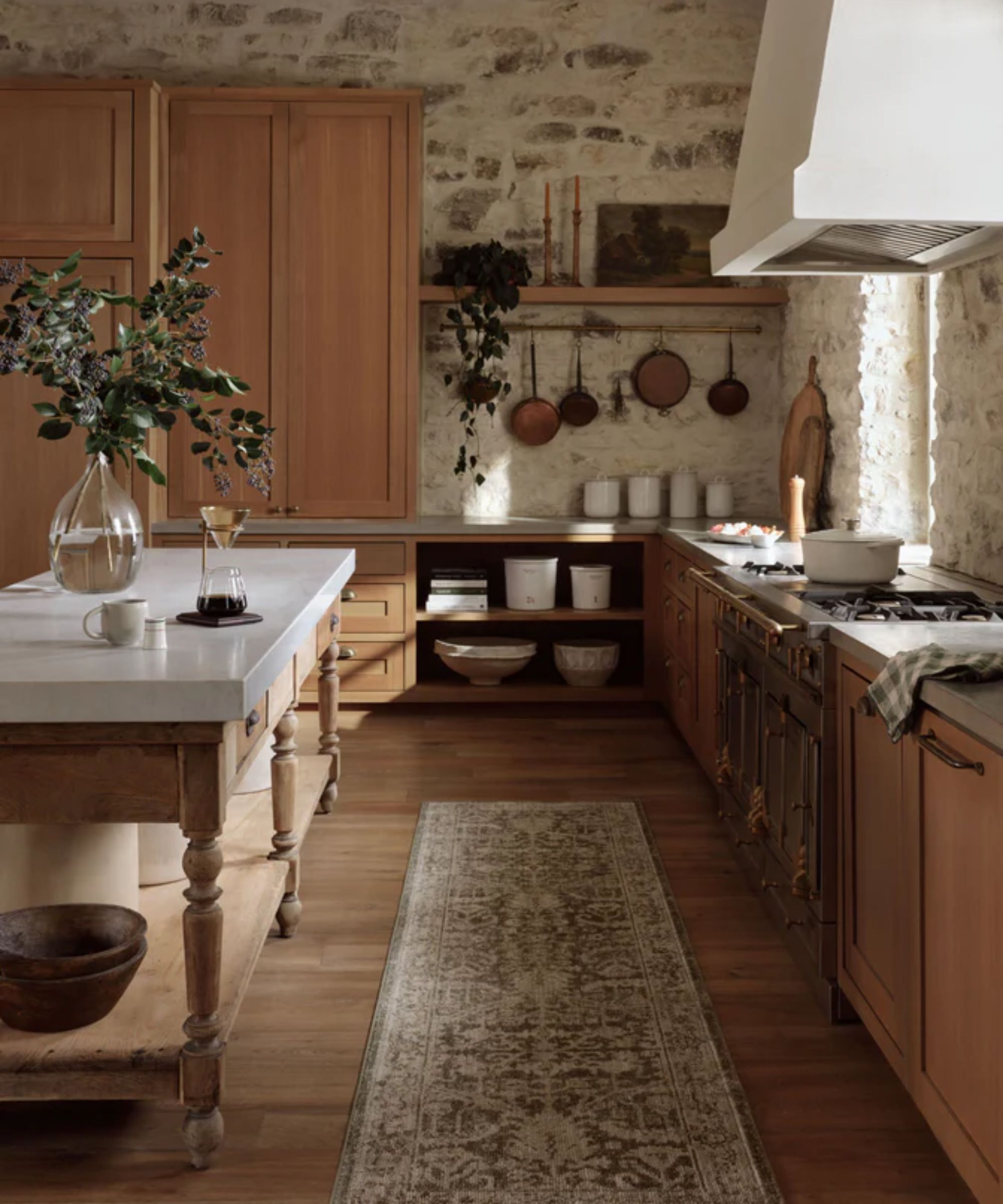 Farmhouse kitchen with exposed stone walls, oak cabinets, plaster hood, wooden work island with marble countertop and vintage runner rug