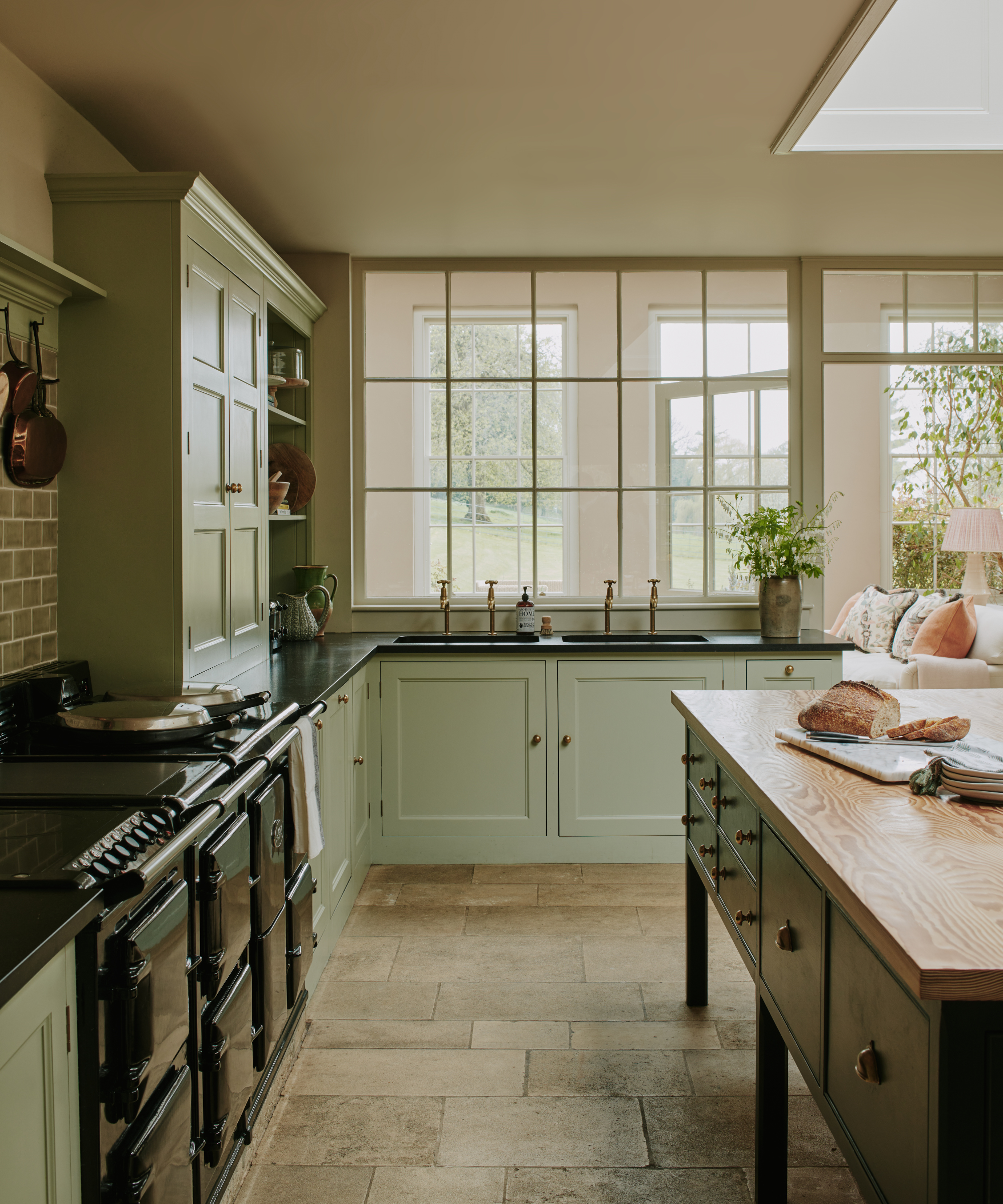 a large kitchen with sage green cabinets, a freestanding island with a wood panel top, a large oven and windows overlooking the garden
