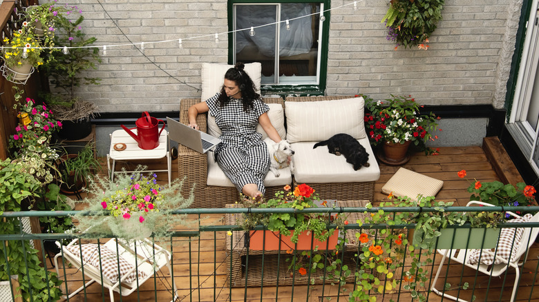 A woman sits with her dog on her terrace, surrounded by flowering plants.