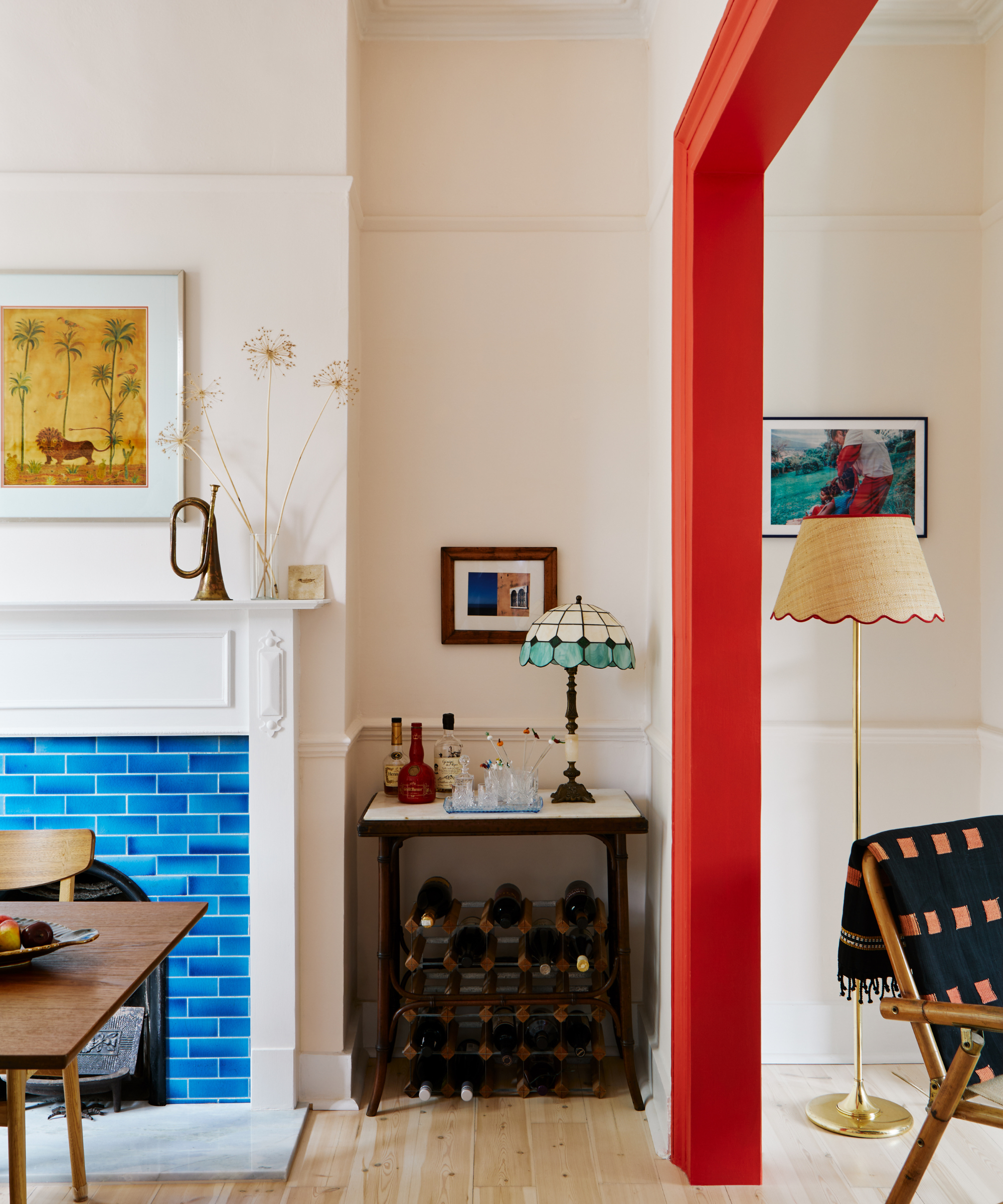 a bright red door frame separating two rooms. To the left is a dining room with a bright blue tile fireplace and a wine rack under a small bar table.