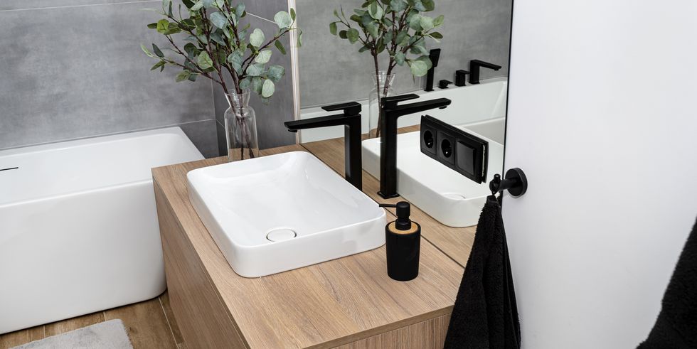 A modern bathroom sink in a closet with a matte black faucet, exposed mirror and artificial flowers.