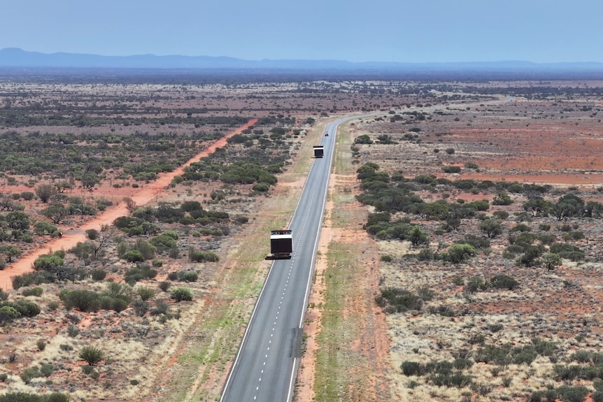 Trucks drive along an outback highway, transporting parts of a modular home.
