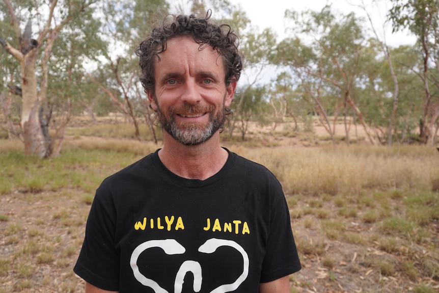 A man with curly hair smiles into the camera, his T-shirt says: Wilya Janta