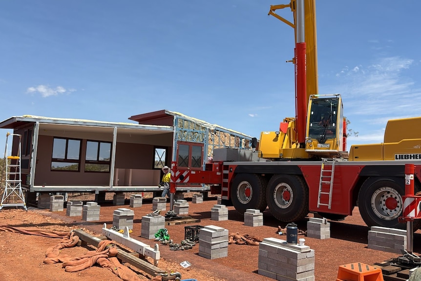 Heavy machines on red earth work on building a modular house.