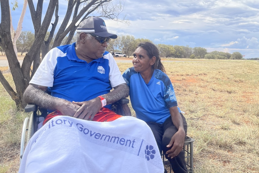 A man in a wheelchair looks at a woman next to him, they smile at each other.