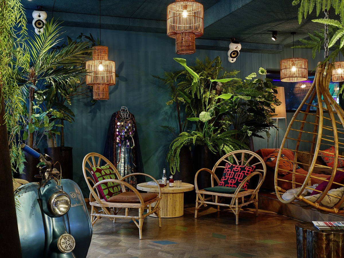 Dark blue walls, green plants and wicker furniture in the lobby of the 25h Hotel The Trip